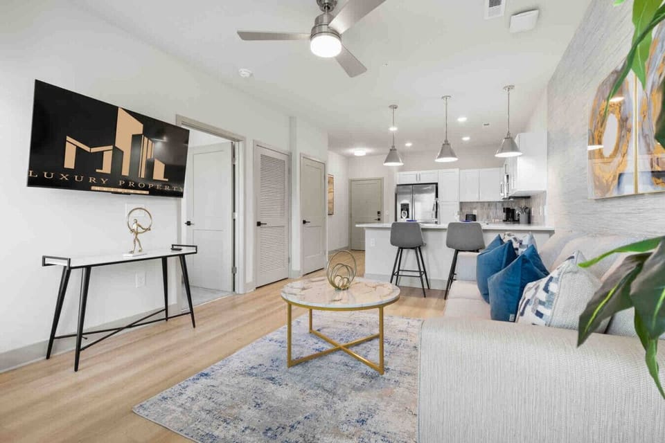 Modern Open-Concept Living-Relax in our stylish, open-concept space. The living area with a smart TV and comfortable sofa flows seamlessly into a modern kitchen with a breakfast bar, perfect for a quiet night in or entertaining guests.