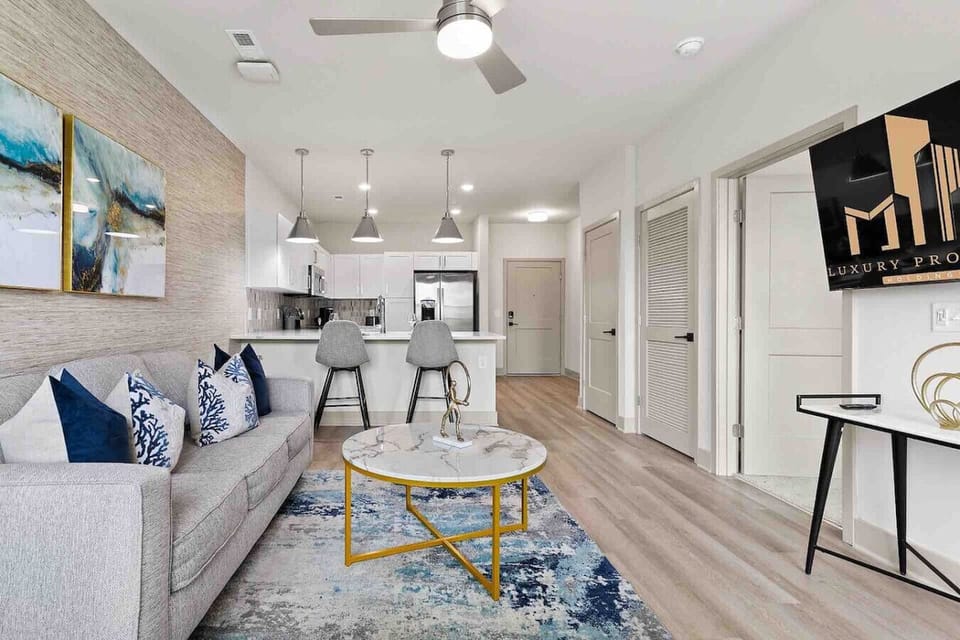 Open-Concept Living & Kitchen-Stylish living area with a cozy sofa, modern décor, and TV flows into a sleek kitchen with breakfast bar seating. Bright, open layout designed for comfort and convenience.