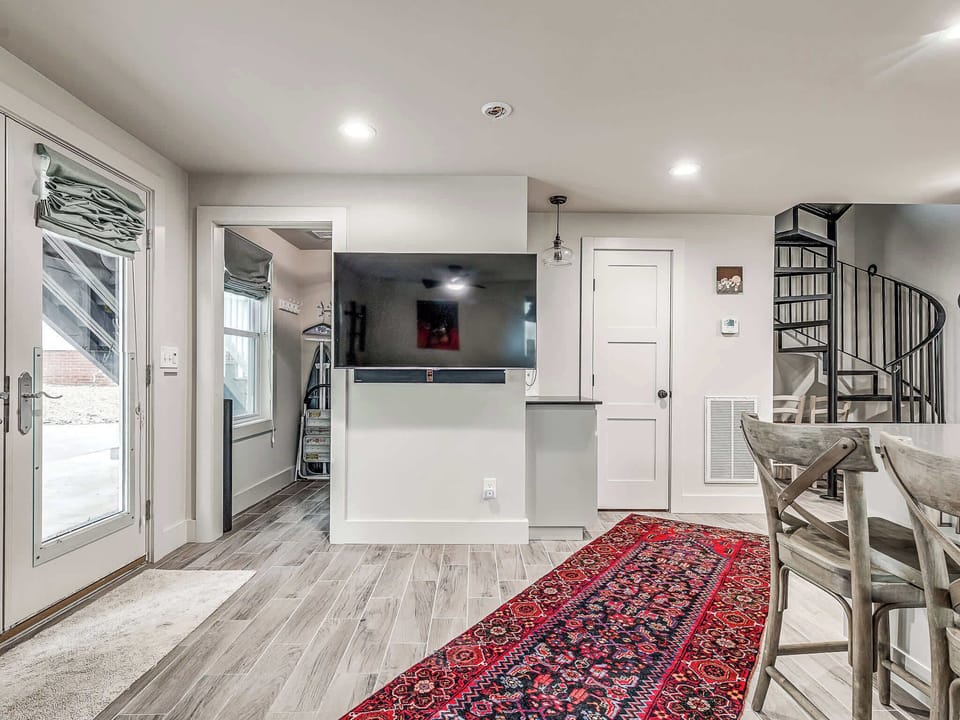 This is the stylish entrance to the guest house. The space features a flat-screen TV, a spiral staircase leading to the upper level, and a doorway to a convenient laundry area.