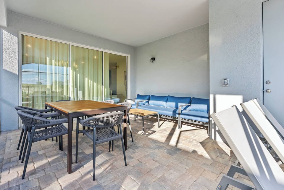 Experience this inviting outdoor space with stylish furniture and warm stone pavers. Dine al fresco at the large table, surrounded by cozy seating and plenty of natural light pouring in through the glass doors.