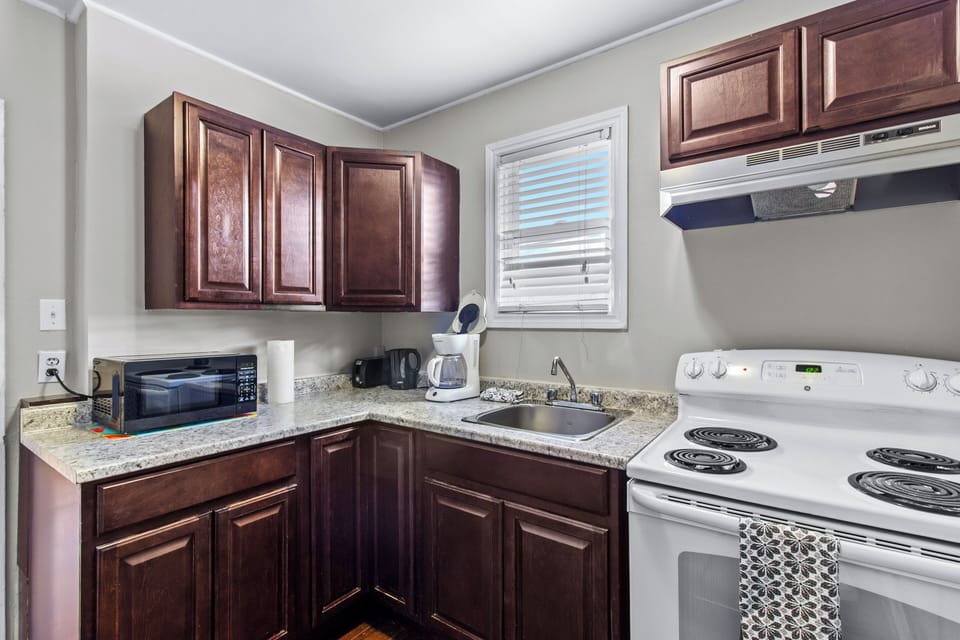 Fully equipped kitchen with dark wood cabinetry, clean white appliances, coffee maker, and microwave. Perfect for home-cooked meals.