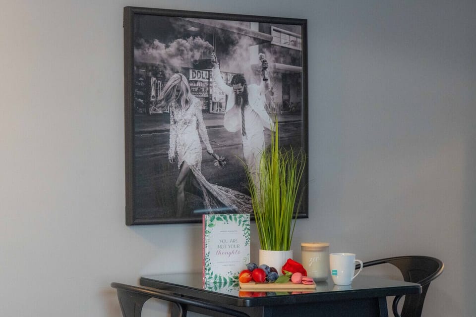 Inspire your stay! Our chic dining nook features a unique black and white art piece, a `Mindful in Minutes` journal, and a selection of fresh fruits & macarons. Enjoy a calming `zen` candle and hot tea, perfect for reflection or a delightful treat