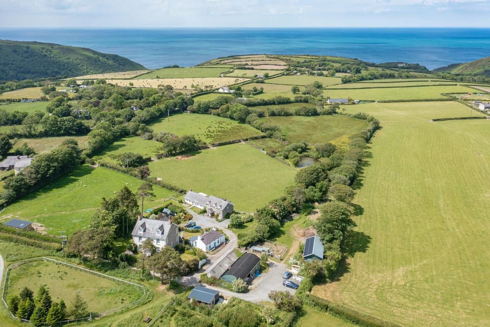 Aerial view of cottage surrounded by fields with sea views