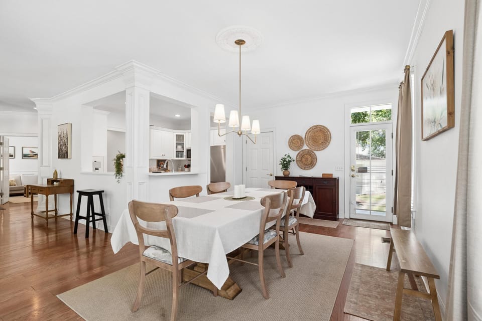 Dining area with a rectangular table covered in a white cloth, six wooden chairs, and a pendant light overhead.