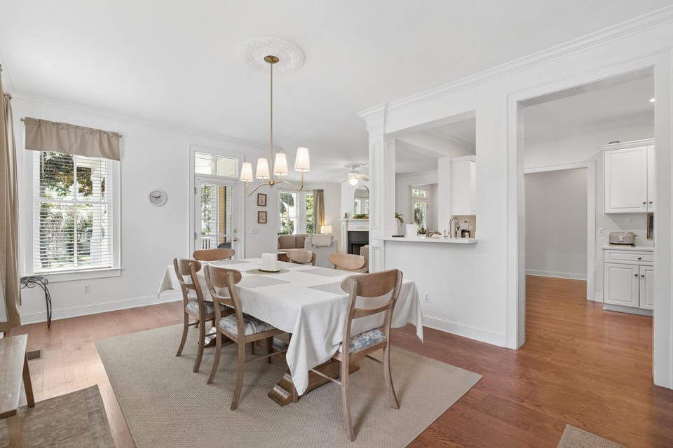 Dining room features a six-seat wooden table with a white cloth, pendant light, and hardwood floors.
