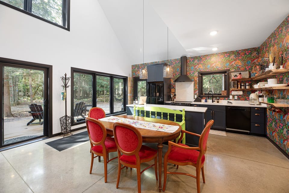 Bright kitchen-dining space w/ bold backsplash, dark cabinetry, & a long table set beneath warm pendant lights.