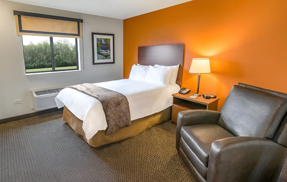 Relax in plush bedding beside a comfy chair and window views.