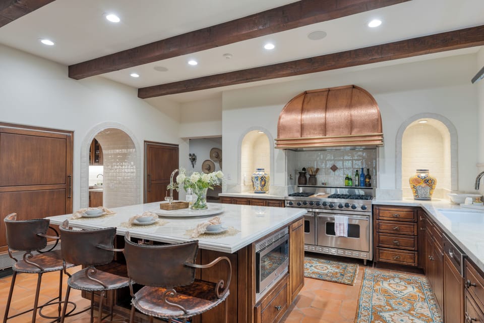 Gourmet kitchen with a large center island, a professional-grade range with a striking copper hood, and rich wooden cabinetry.
