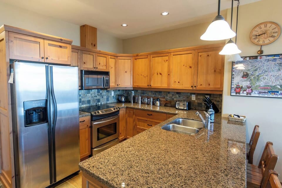 This bright kitchen features stainless steel appliances, wooden cabinets, and granite countertops. A breakfast bar and a decorative map add a unique, inviting touch to the space.