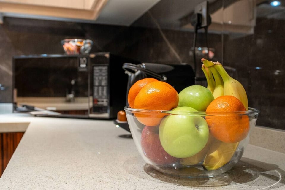 Glass fruit bowl with apples, bananas, and oranges on kitchen countertop.