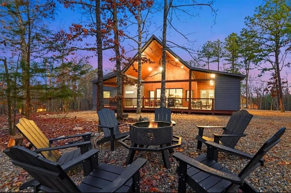 Modern cabin with fire pit seating surrounded by tall pines at sunset