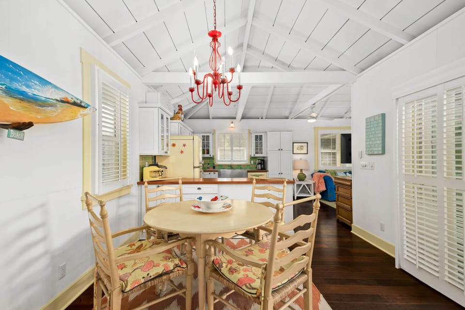 Sunny cottage dining with red chandelier, tropical seats, and vintage kitchen.