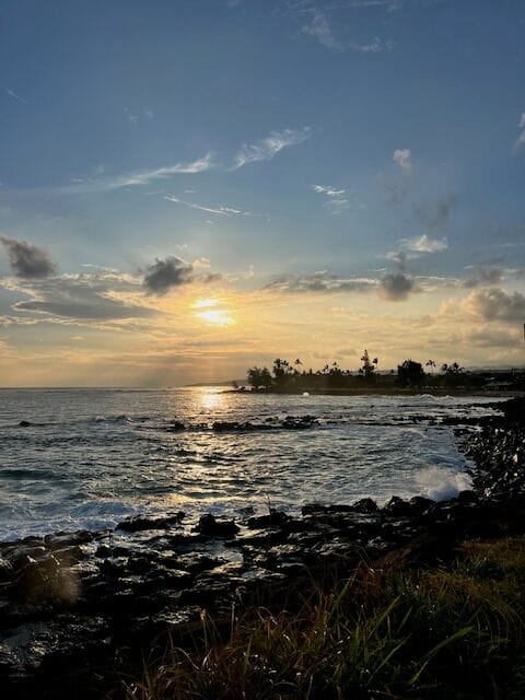 Soft Kauai sunset over rocky tide pools; palms etched on the horizon as the ocean turns to glass.