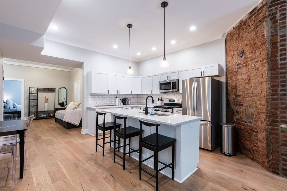 Pull up a sleek black barstool to the bright white kitchen island for your morning coffee. The stainless steel appliances perfectly complement the historic charm of the exposed brick pillar.