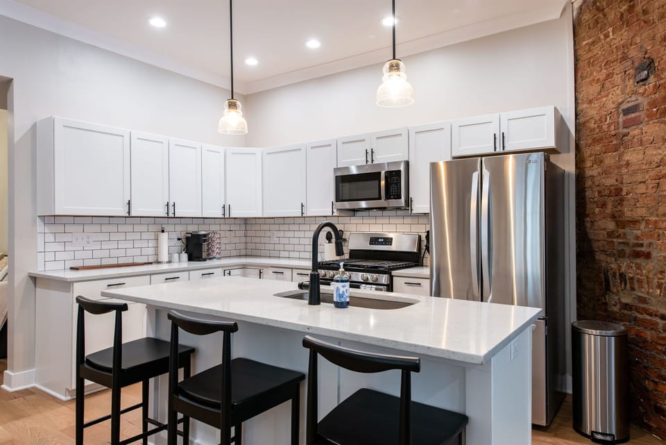 Wash up easily at the sleek black sink faucet perfectly centered on the massive white quartz island. Clear glass pendant lights add a touch of brilliant illumination from above.