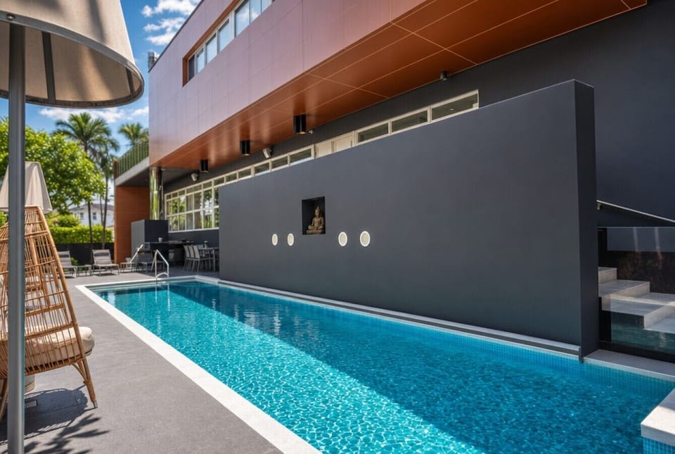 Contemporary outdoor space with a long narrow lap pool, striking dark grey privacy wall, and wicker seating