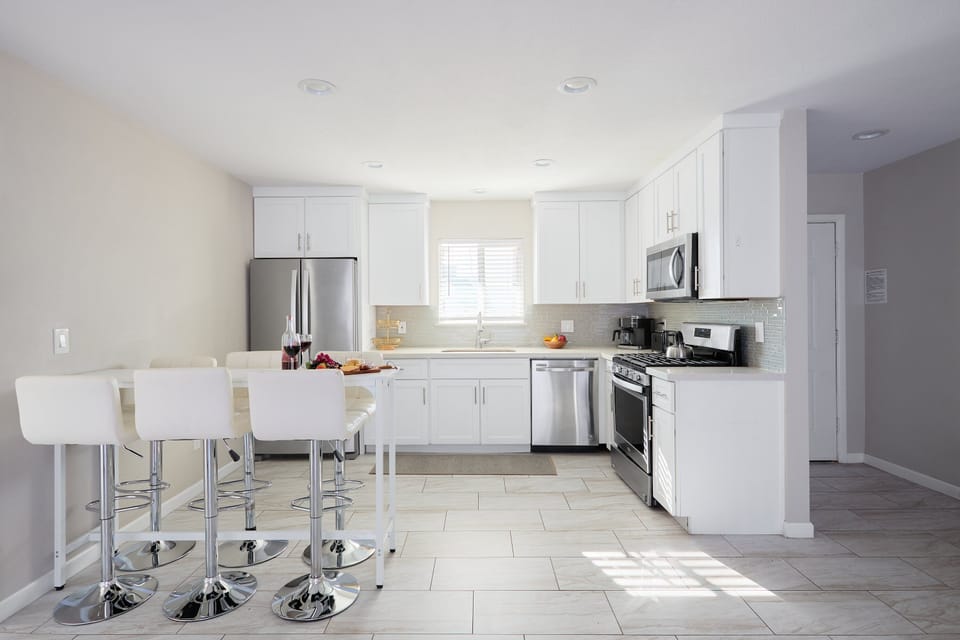 Bright kitchen with white cabinets and countertops, stainless steel appliances, and a dining table with seating for six.