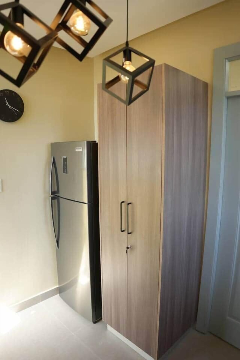 Sleek kitchen corner with a modern stainless steel fridge, tall pantry cabinet, and geometric pendant lights—smart, stylish, and ready for your stay.