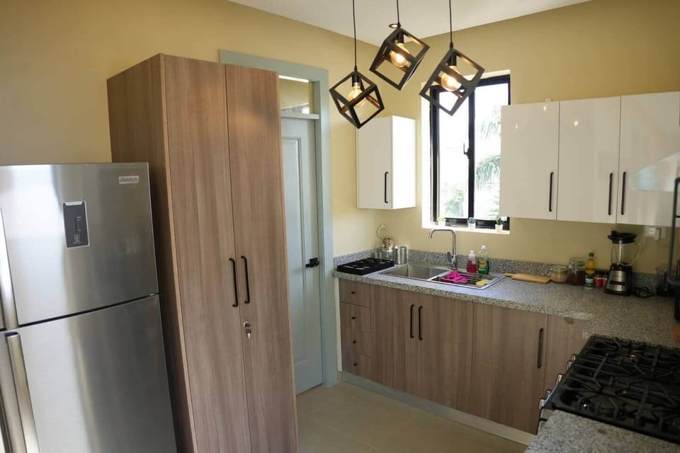 Stylish, fully equipped kitchen with granite countertops, modern appliances, warm wood finishes, and statement lighting—everything you need to cook and feel at home.