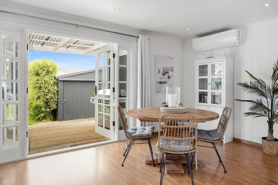 Gather around the timber dining table beneath soft natural light, where French doors open to the deck for seamless indoor-outdoor meals and breezy coastal ambience.