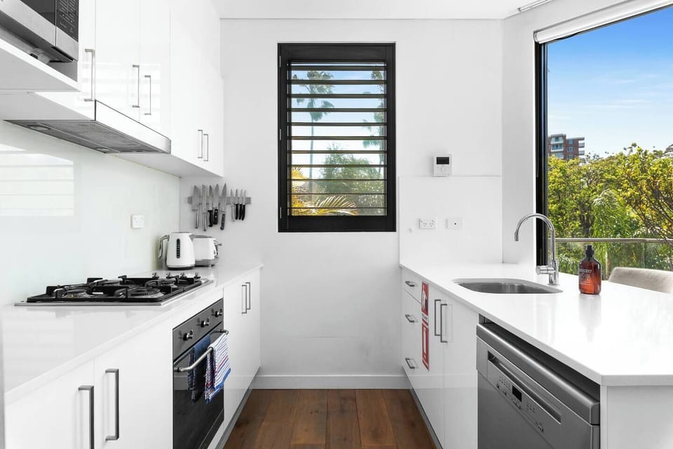 Prepare meals in a sleek galley kitchen with a full suite of appliances, a gas cooktop, cooking essentials, and leafy outlooks.
