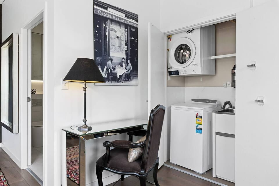 Tucked beside the bathroom, a dedicated workspace provides a quiet spot to catch up on emails, while concealed laundry facilities with a washer, dryer, and sink add everyday convenience.