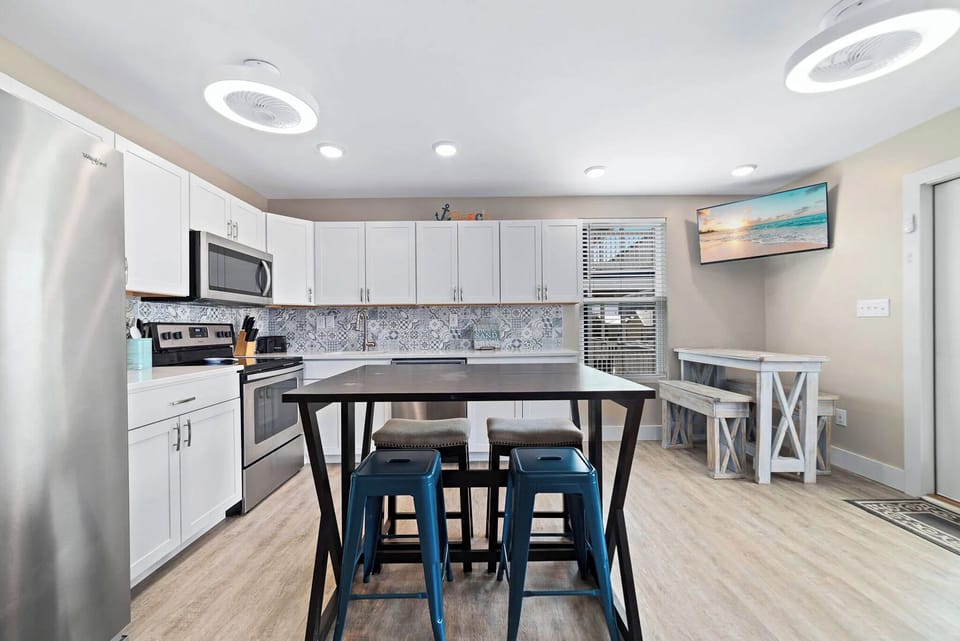 Modern kitchen featuring stainless appliances, stylish bar seating, and a cozy dining area with a TV
