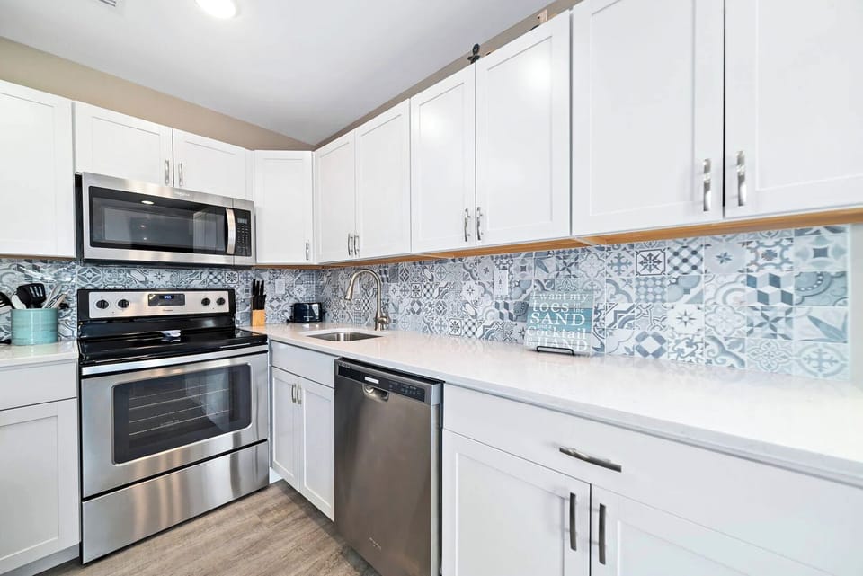 Stylish kitchen featuring stainless appliances, white cabinetry, and a colorful tiled backsplash