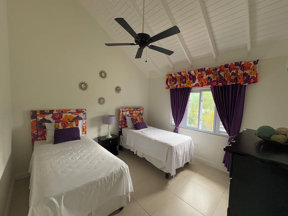 Twin bed bedroom equipped with ceiling fan, AC unit, wood dresser and closet