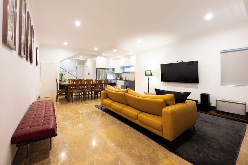 Open-plan living and dining area, sofa facing a wall-mounted TV, and dining area