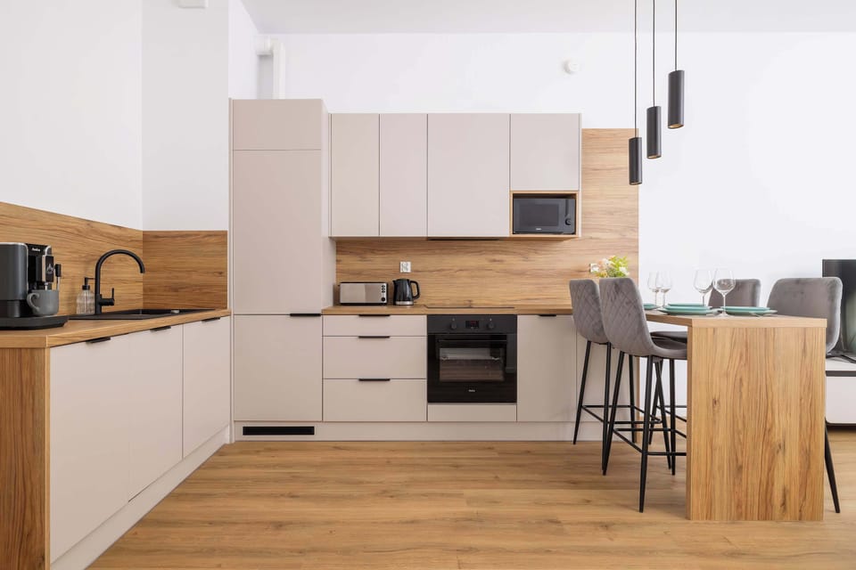 A modern kitchen with light wooden cabinets and white countertops. There’s a stove, oven, and other kitchen appliances arranged in a clean, compact design.