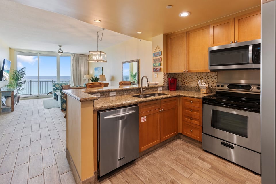 Your fully-equipped kitchen flows seamlessly into the living space, where ocean views through floor-to-ceiling windows create the perfect backdrop for cooking.