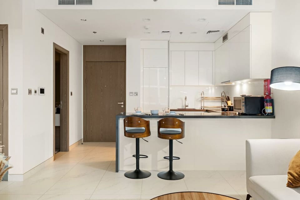 Modern open kitchen with breakfast bar, wooden stools, and entryway view.