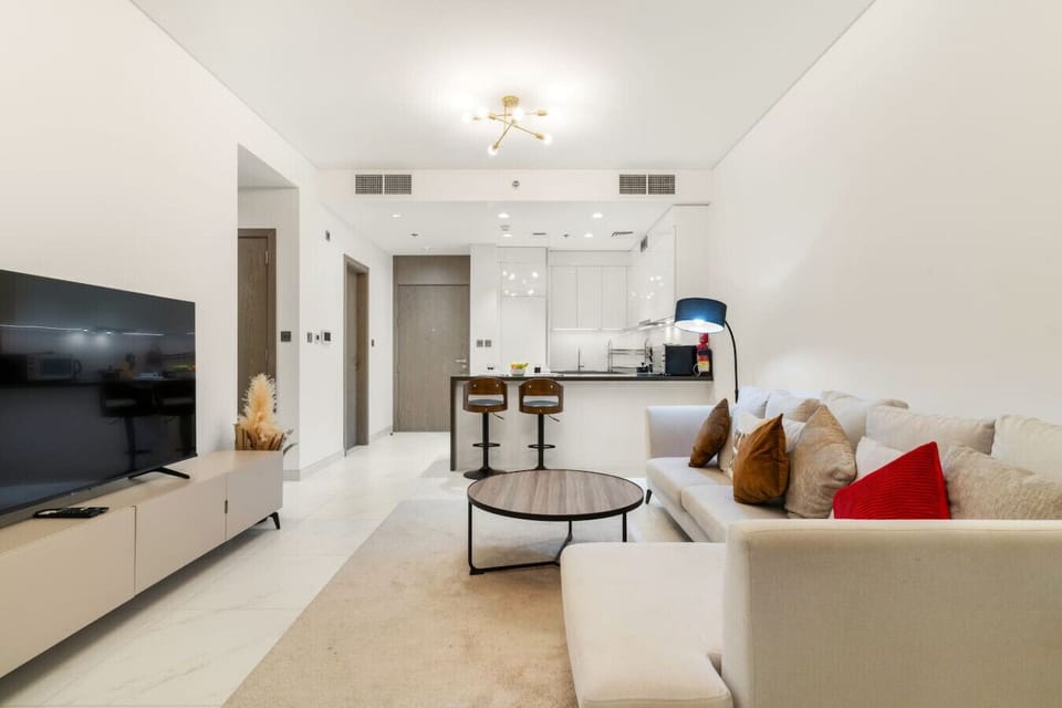 Stylish lounge with TV, sectional sofa, warm lighting, and open kitchen.