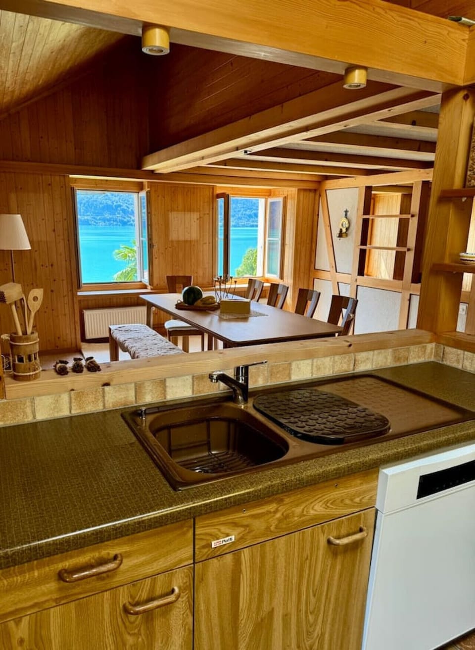 Fully equipped alpine kitchen with sink, dishwasher, and direct view into the dining area and Lake Brienz