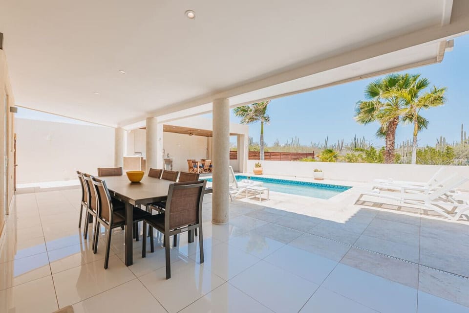 Gather in this bright outdoor area with seating for eight, offering beautiful views of the pool and palm trees, ideal for enjoyable meals and relaxation.