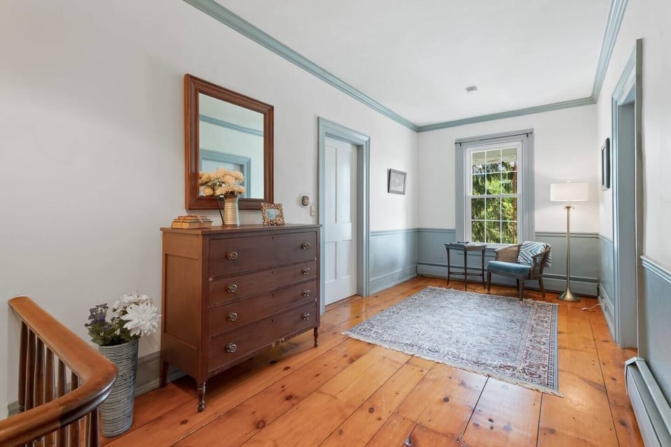 The upstairs landing boasts rich wood floors, classic trim details, and a cozy sitting area. Take a moment to pause and enjoy the natural light streaming through the window. 