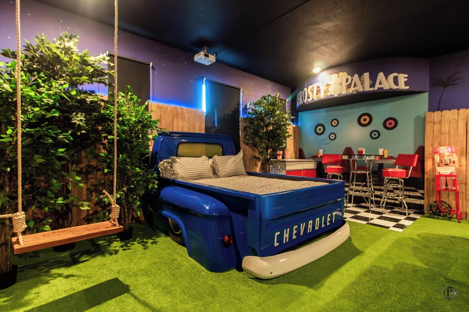50s drive-in room with pickup truck bed, car-seat sofas & movie projector