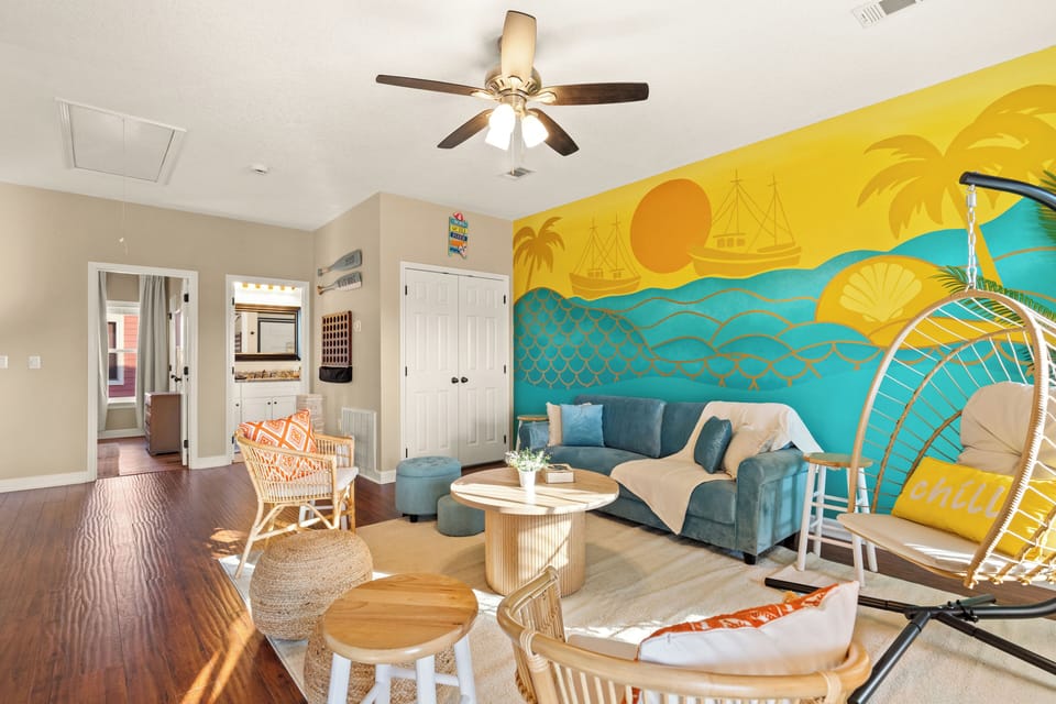 Main living room with a floor-to-ceiling custom coastal mural, Smart TV, comfortable sectional, and the record player that sets the Tahitian Way tone. This is the room everyone gravitates to.