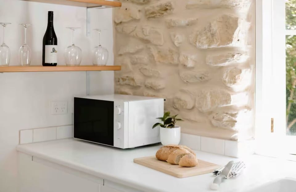 Kitchen bench microwave and glassware, handcrafted stone wall.