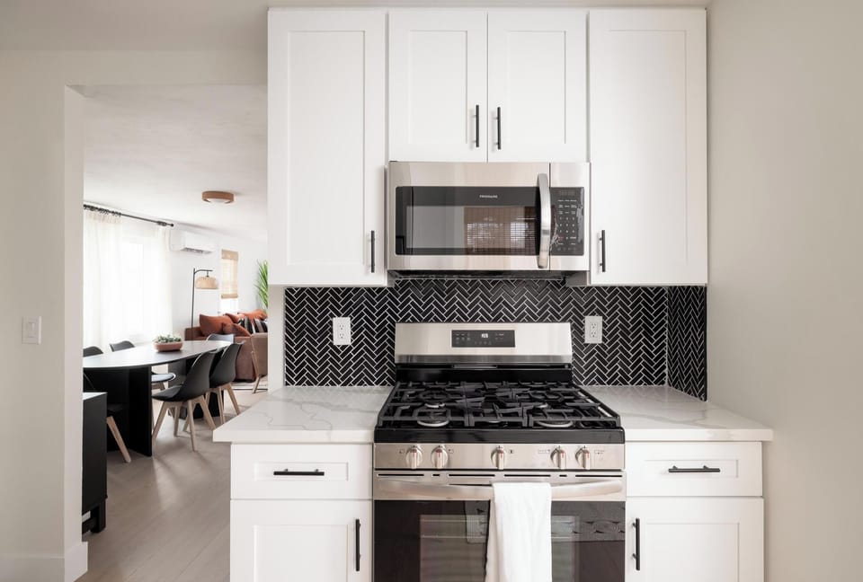 Modern kitchen with stainless steel stove and microwave, sleek backsplash. 