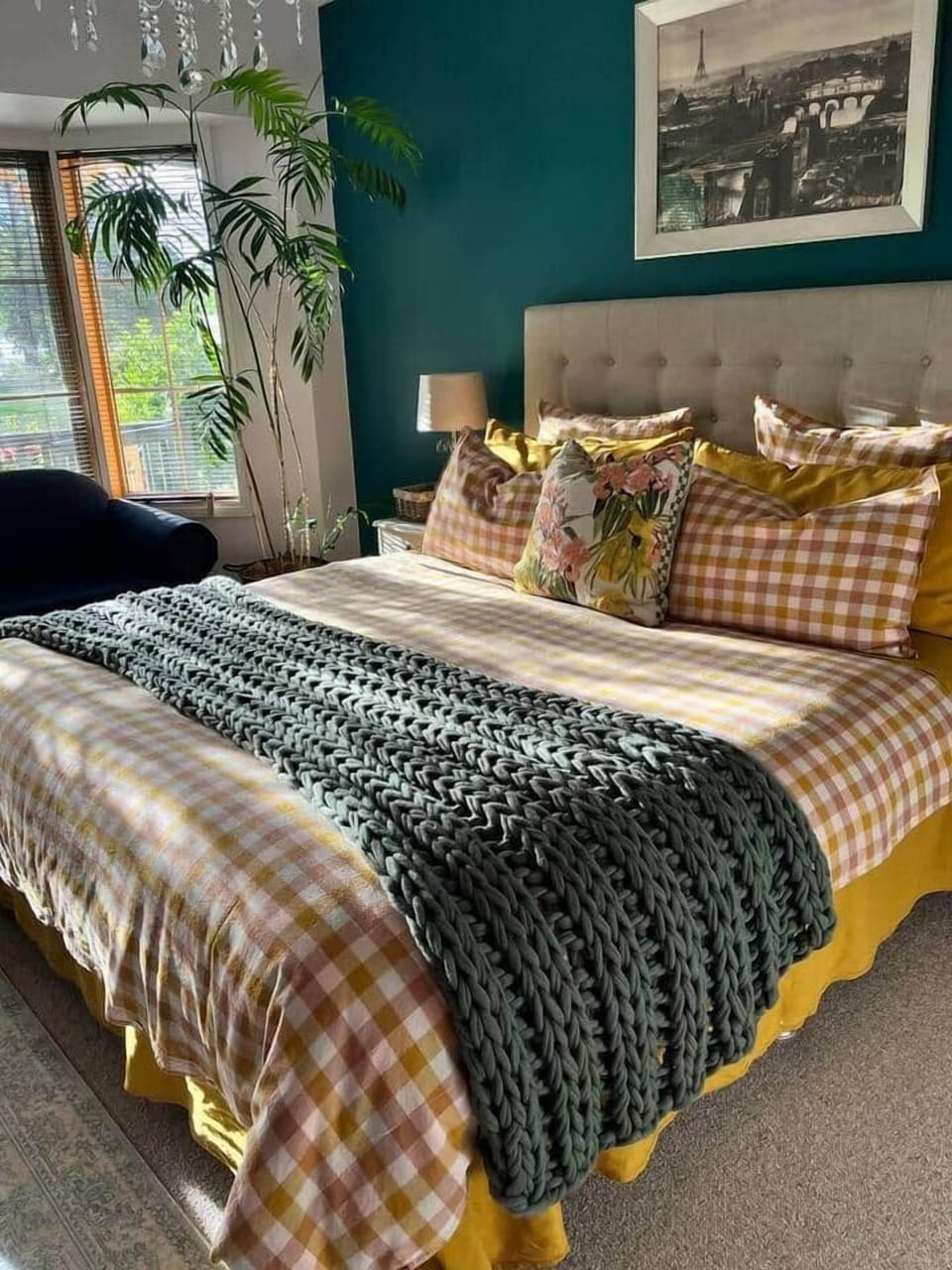 A beautifully dressed king bed with plush check design bedding and sun filtering through the bay window 