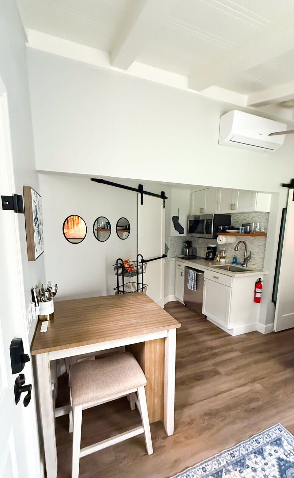 In-unit stacked washer and dryer behind a sliding barn door, steps from a fully equipped kitchen with sink, coffee station, and open shelving - everything for a comfortable extended stay.