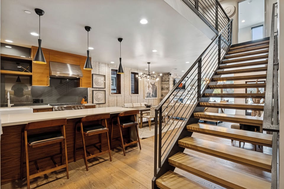 Modern kitchen and staircase area with bar seating and pendant lights