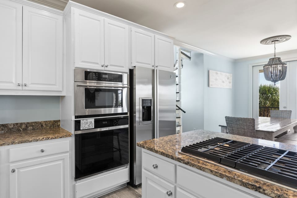 Sleek white kitchen featuring a double door fridge, ovens, and abundant storage.