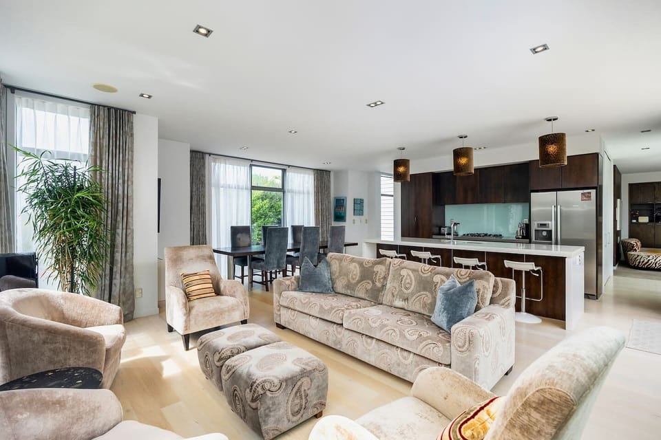 Open plan living, dining and kitchen, with doors opening out to a sunny patio with sun loungers and outdoor dining
