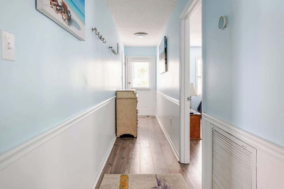 Long coastal hallway with blue walls, wainscoting, and natural light leading to the back door.