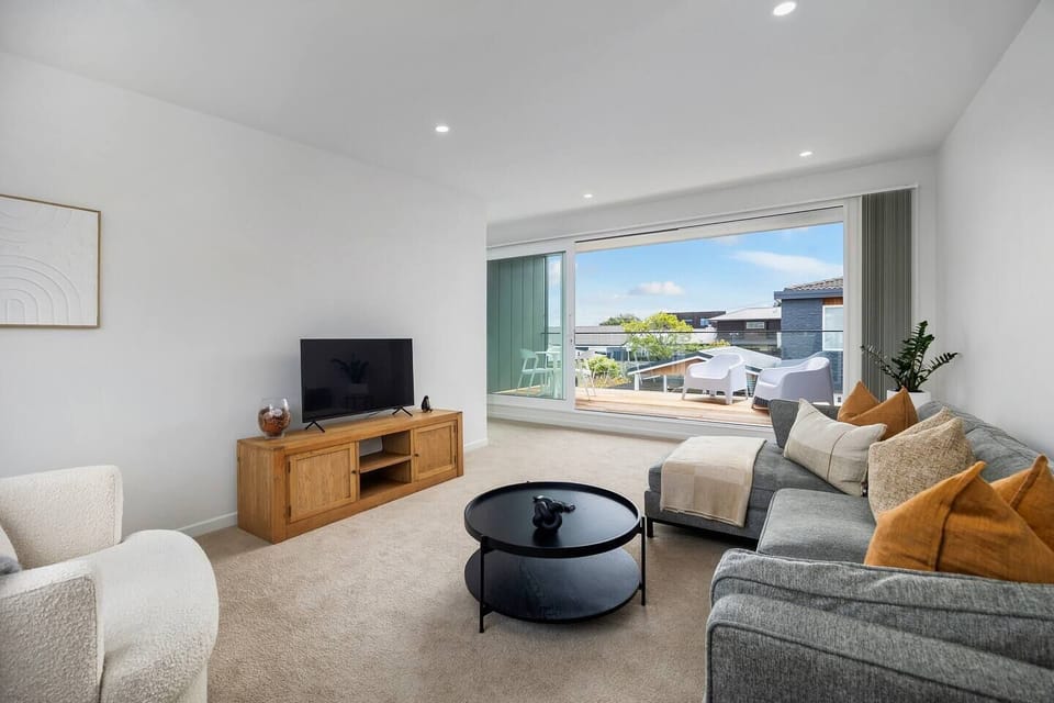 Spacious living room, located upstairs complete with TV, comfy couch, and sliding doors opening out to sunny balcony seating.