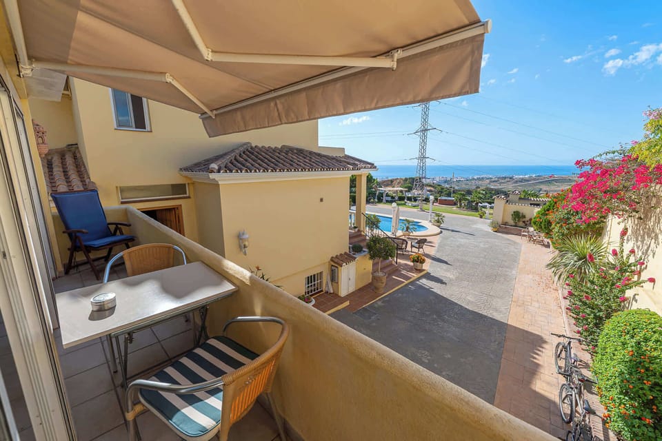 A cozy balcony offers a view of a pool and distant cityscape under a clear sky.