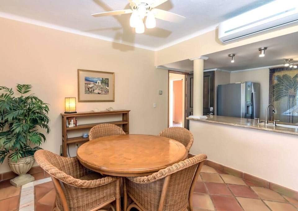 Warm-toned dining area with wicker chairs, round table, and open kitchen with modern appliances.